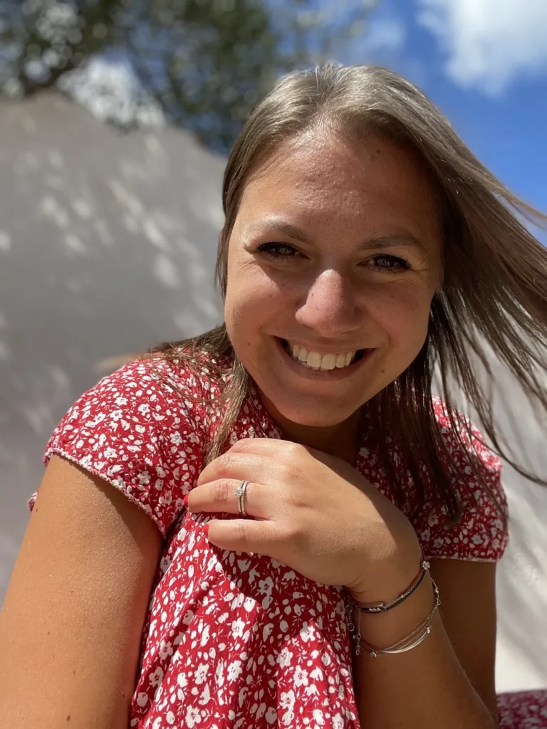Jeune femme de 35 ans en robe rouge à fleur blanche souriante au soleil